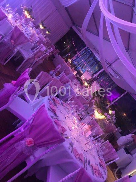 Salle de réception décorée dans des tons roses et violets, avec des tables dressées et des chaises ornées de nœuds.