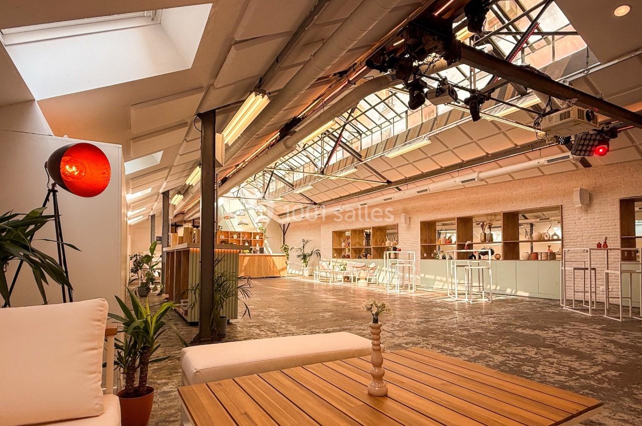 Espace lumineux avec verrière, mobilier en bois et plantes, aménagé pour des événements ou des rencontres conviviales.