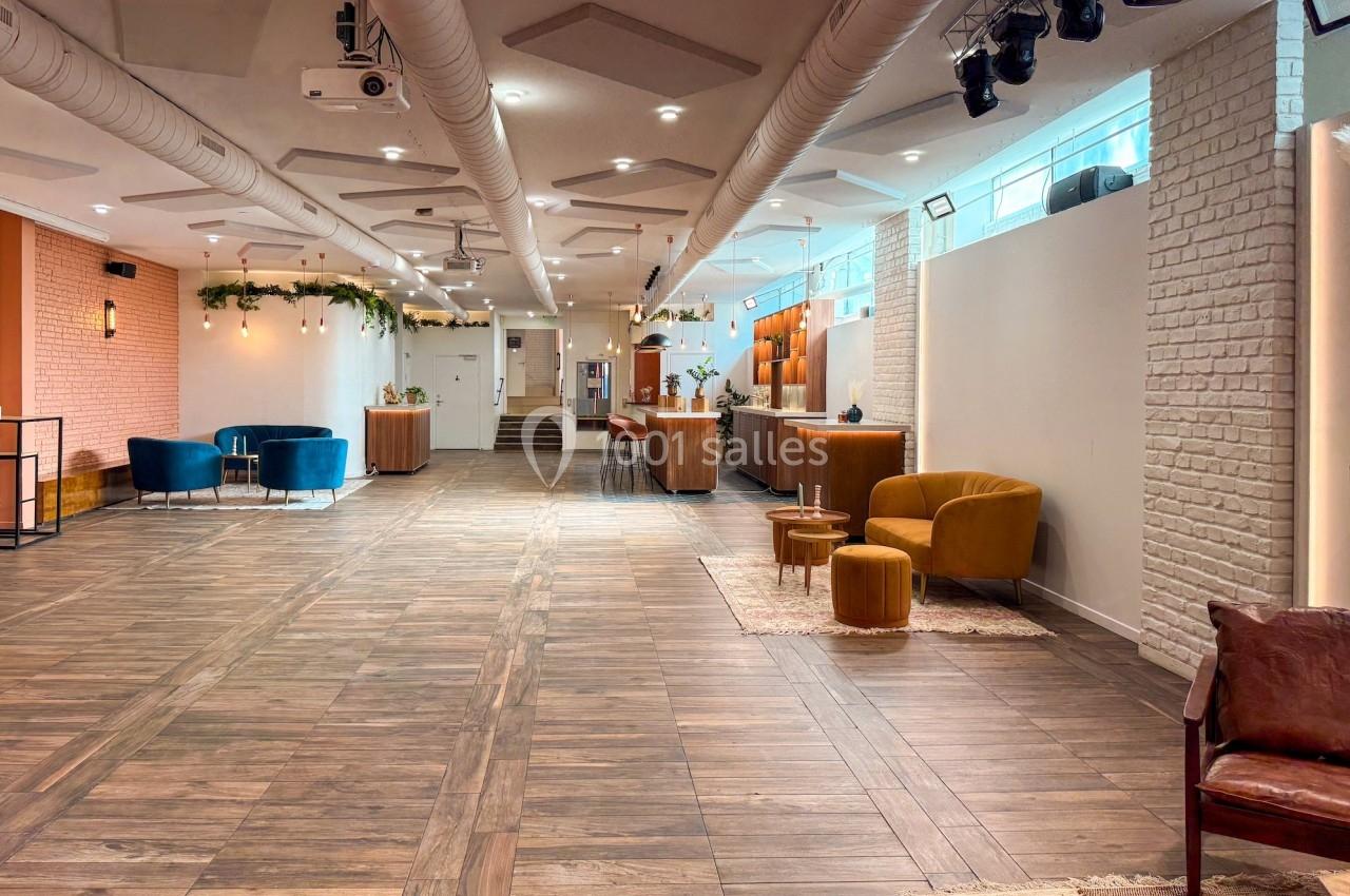 Salle spacieuse avec parquet, mobilier moderne, murs en briques et éclairage chaleureux.