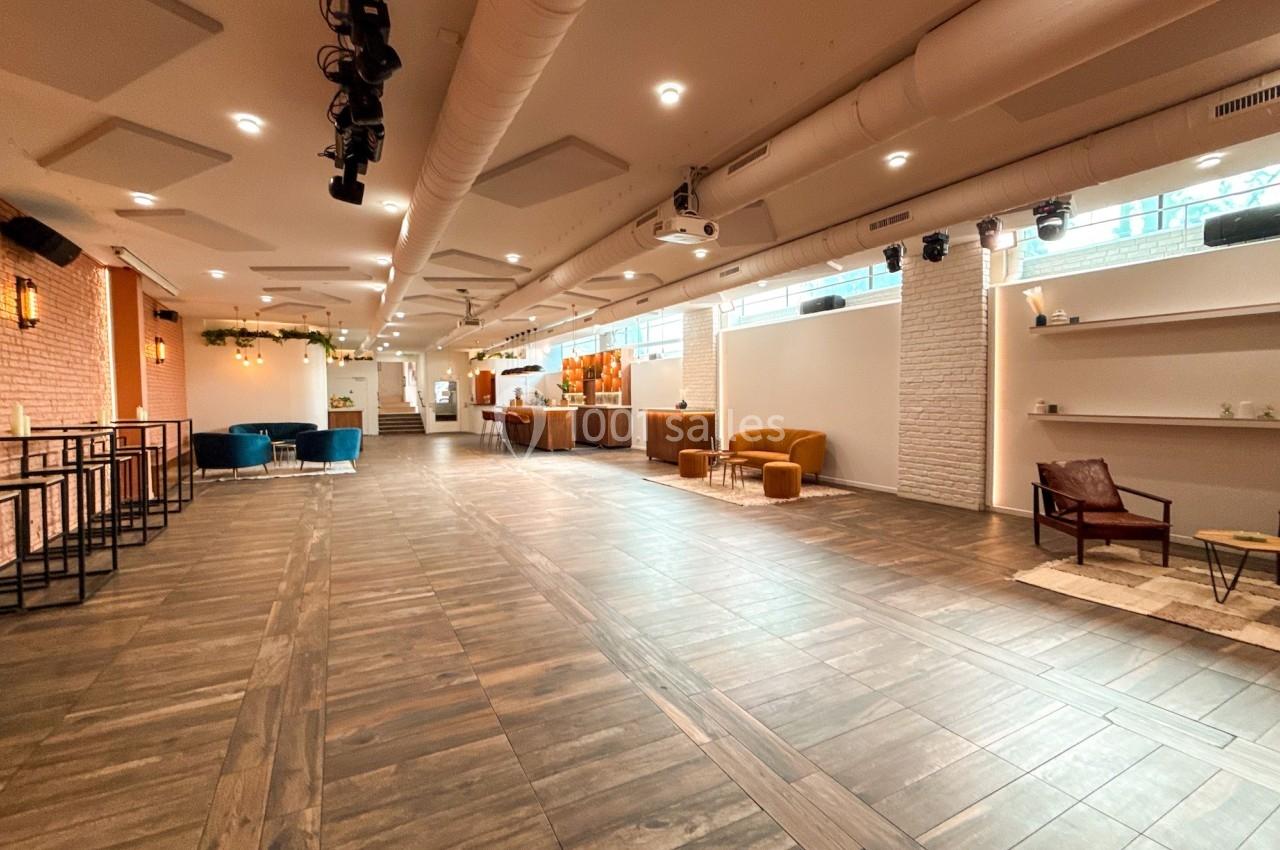 Salle spacieuse avec parquet, murs clairs, mobilier moderne et lumière naturelle provenant de grandes fenêtres.