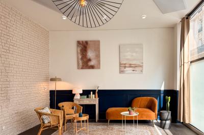 Salon chaleureux avec canapé jaune, fauteuils en rotin, table basse ronde, lampes et décorations murales abstraites.