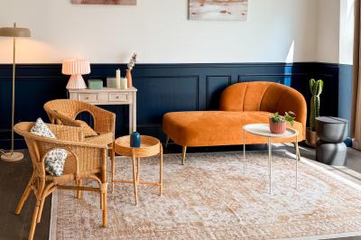 Salon chaleureux avec canapé jaune, fauteuils en rotin, table basse ronde, lampes et décorations murales abstraites.