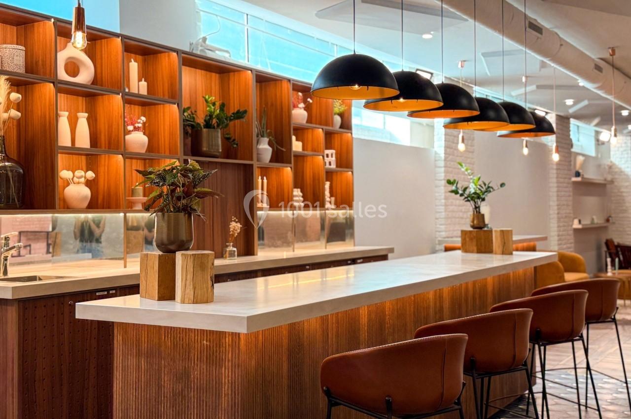 Intérieur d'un café moderne avec un comptoir en bois, des étagères décorées et des suspensions lumineuses noires.