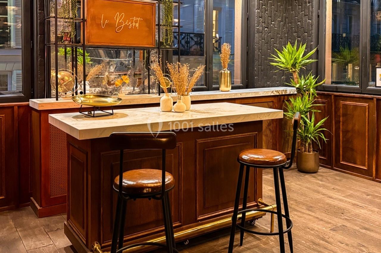 Cuisine moderne avec îlot central en bois, tabourets, plantes vertes et décoration chaleureuse dans un espace lumineux.