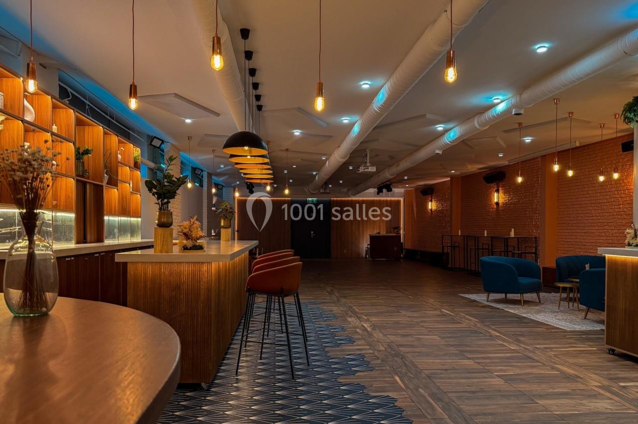 Salle moderne avec éclairage chaleureux, mobilier en bois et sièges colorés, combinant parquet et carrelage géométrique.