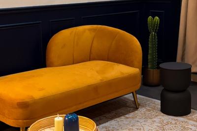 Salon chaleureux avec canapé jaune, fauteuils en rotin, table basse ronde, lampes et décorations murales abstraites.