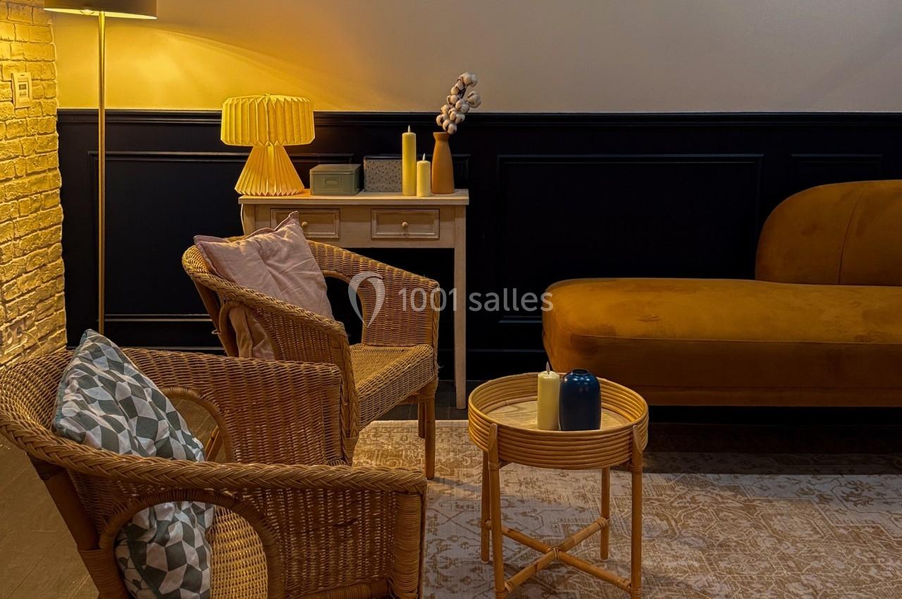 Espace salon chaleureux avec fauteuils en rotin, table basse, canapé jaune moutarde et éclairage tamisé.