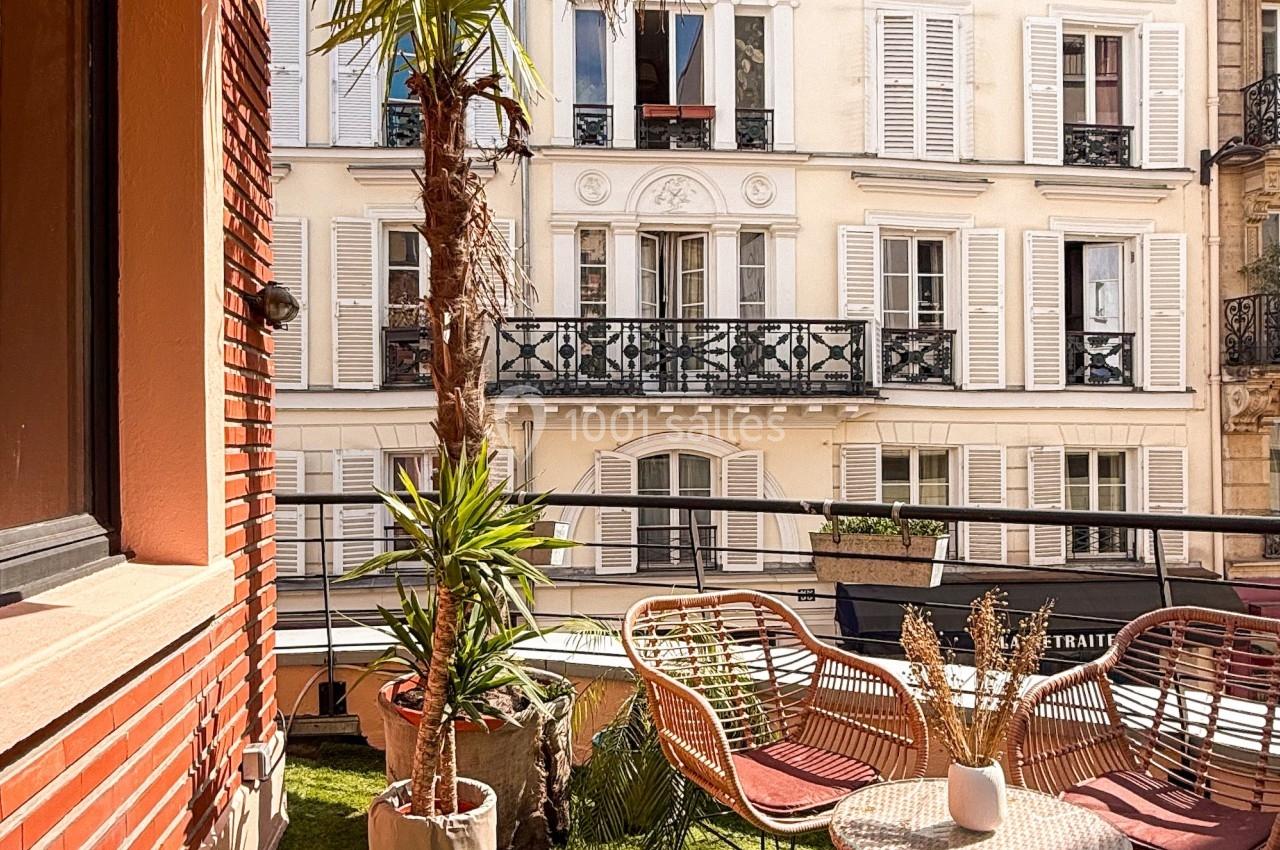 Terrasse avec gazon artificiel, mobilier en rotin, plantes et vue sur des immeubles parisiens aux façades claires.