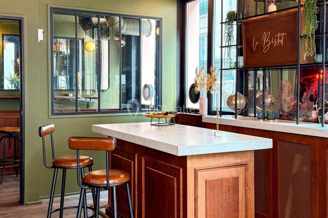 Comptoir en bois avec tabourets hauts, entouré de miroirs et de décorations végétales dans un espace intérieur lumineux.