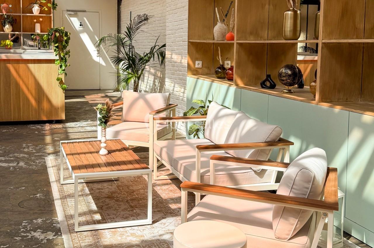 Espace lumineux avec fauteuils modernes, table basse en bois, étagères décoratives et plantes dans un intérieur industriel.