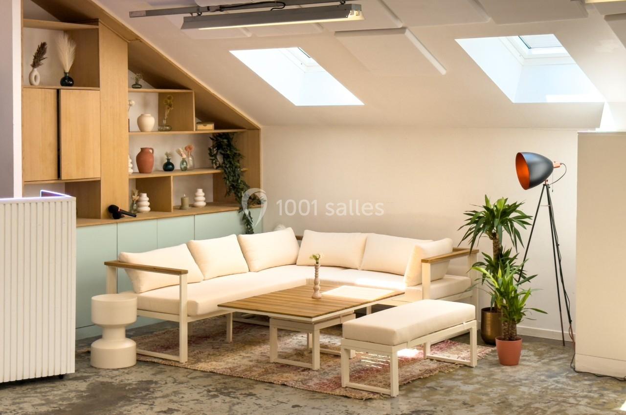 Salon lumineux sous combles avec canapé d'angle beige, table basse en bois, plantes et étagères décorées.