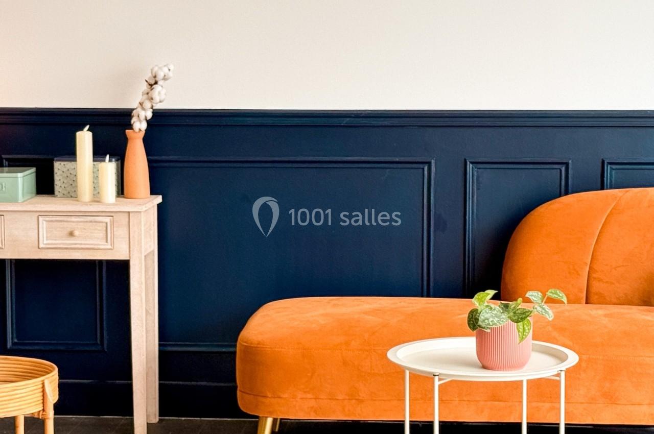 Canapé orange avec table basse blanche, plante en pot et décoration minimaliste sur fond de mur bleu et blanc.