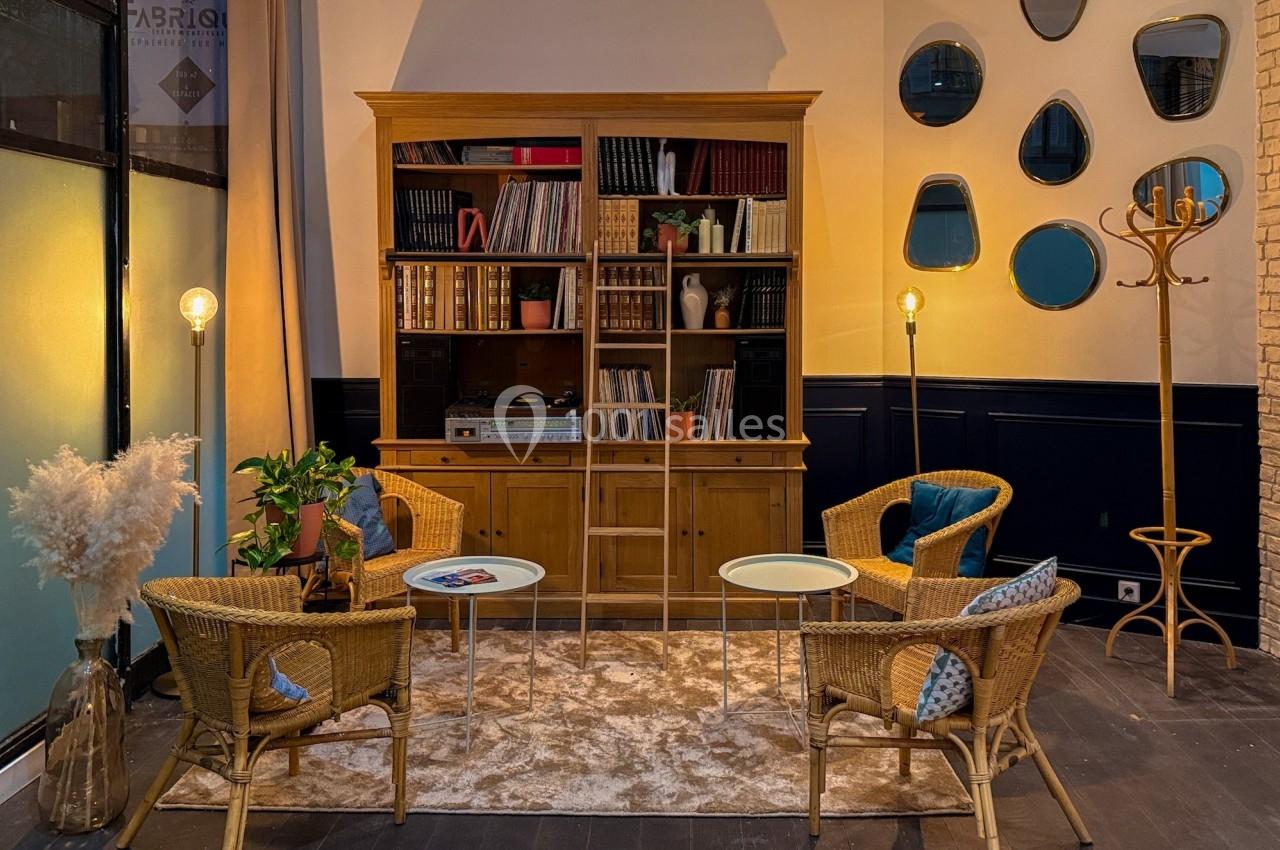 Salon chaleureux avec étagère en bois, fauteuils en rotin, tables basses, tapis beige et lampes d'ambiance.