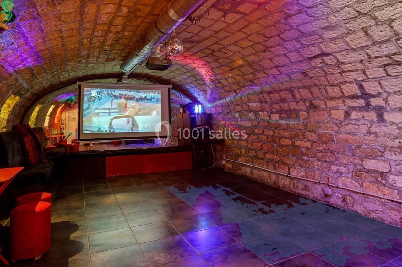 Salle voûtée en pierre avec un écran de projection, éclairage coloré et mobilier minimaliste.