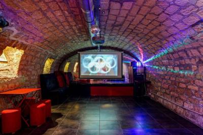 Bar avec comptoir rouge éclairé, tabourets hauts, murs en pierre et briques, décorations murales et étagères avec bouteilles.