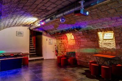 Bar avec comptoir rouge éclairé, tabourets hauts, murs en pierre et briques, décorations murales et étagères avec bouteilles.