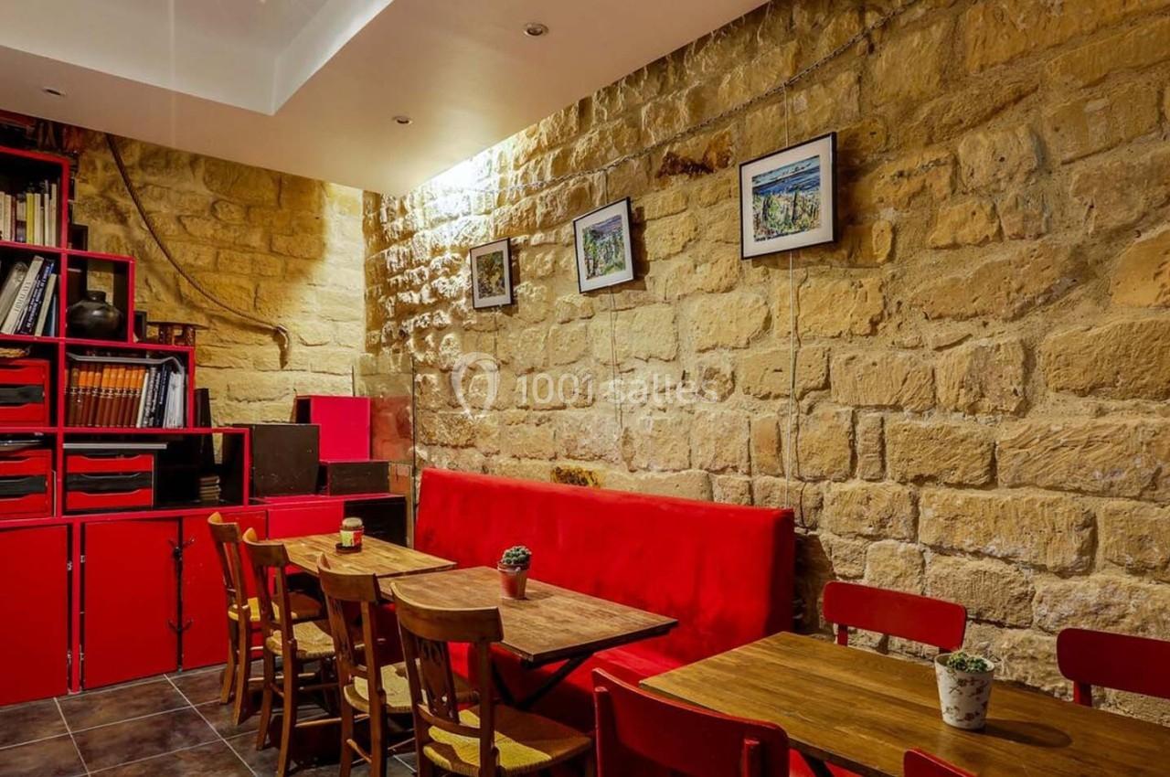 Salle avec murs en pierre, étagères rouges, tables en bois, chaises assorties et décoration murale.