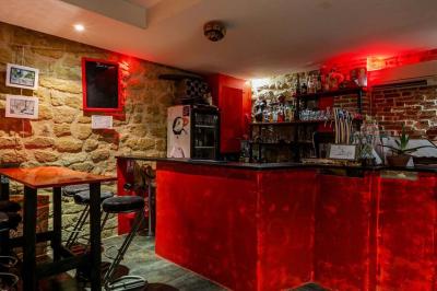 Bar avec comptoir rouge éclairé, tabourets hauts, murs en pierre et briques, décorations murales et étagères avec bouteilles.