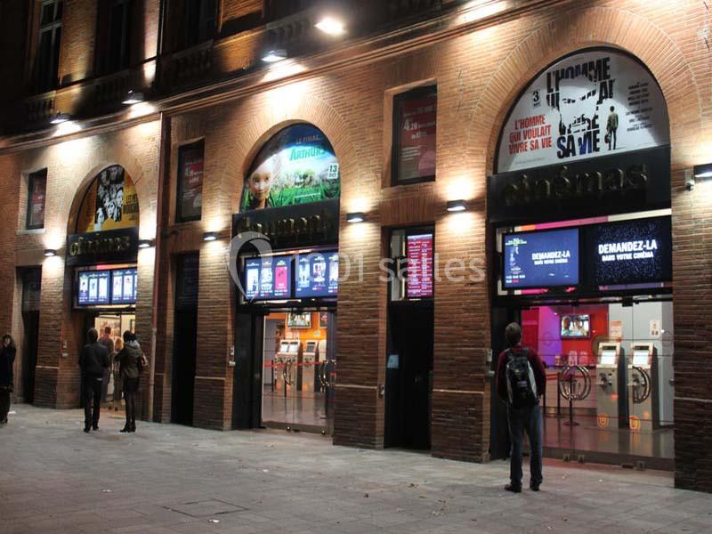 Façade d'un cinéma de nuit avec plusieurs affiches lumineuses et quelques personnes devant l'entrée.
