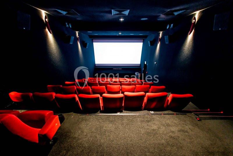 Salle de cinéma vide avec des rangées de sièges rouges et un écran blanc allumé à l'arrière-plan.