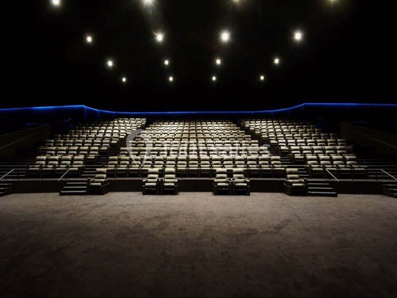 Salle de cinéma vide avec des rangées de sièges inclinables et un éclairage tamisé au plafond.
