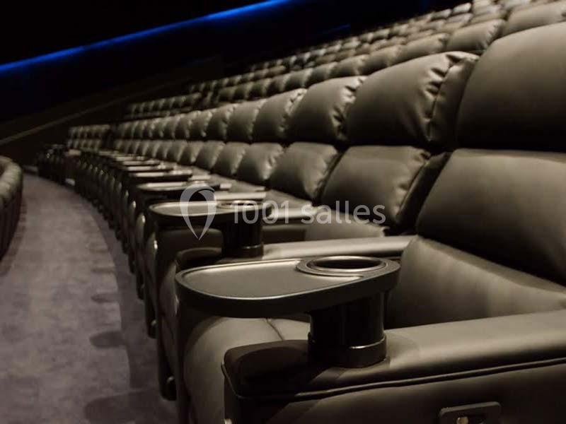 Rangées de fauteuils de cinéma en cuir noir avec porte-gobelets intégrés, dans une salle vide.