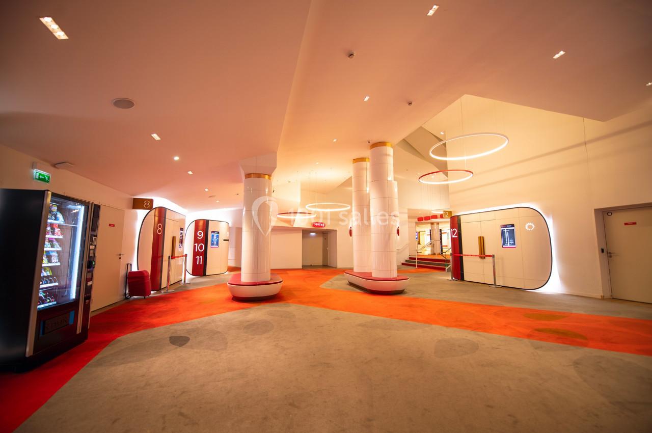 Hall moderne avec moquette colorée, colonnes blanches, éclairage circulaire suspendu et distributeur automatique à gauche.