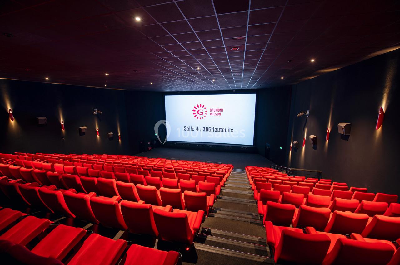 Salle de cinéma moderne avec rangées de fauteuils rouges vides et écran affichant ’Salle 4 - 386 fauteuils’.