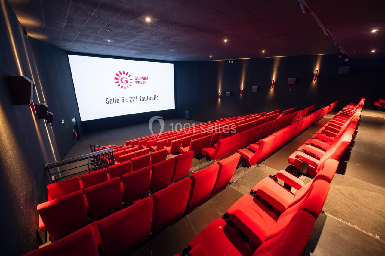 Salle de cinéma moderne avec rangées de fauteuils rouges et écran affichant ’Salle 5 : 221 fauteuils’.