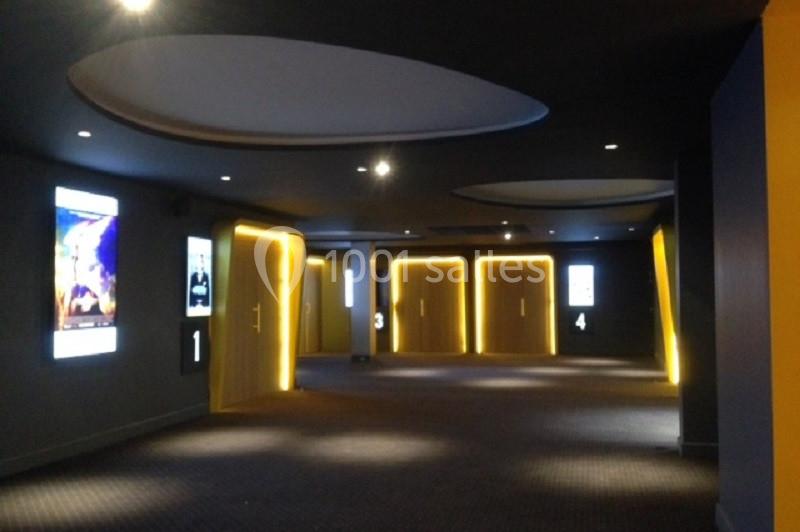 Couloir d'un cinéma avec portes numérotées et affiches lumineuses sur les murs sombres.