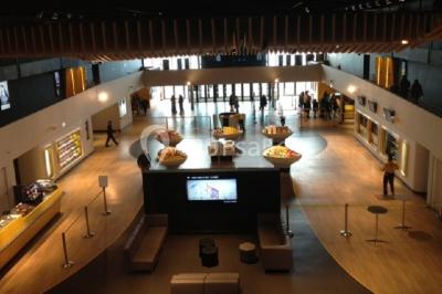 Salle vide avec moquette sombre, grande baie vitrée et structures métalliques visibles en arrière-plan.