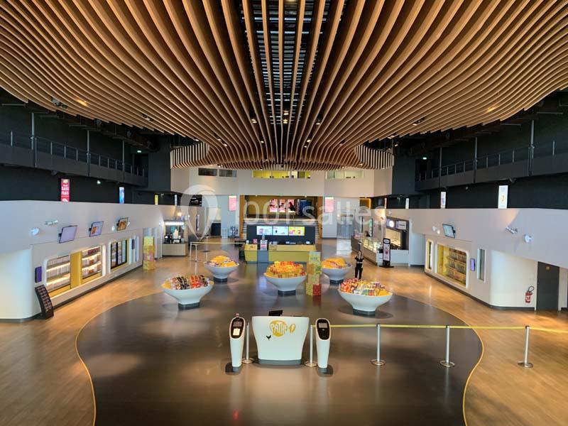 Hall spacieux d'un cinéma avec comptoirs de snacks, présentoirs de confiseries et plafond en bois ondulé.