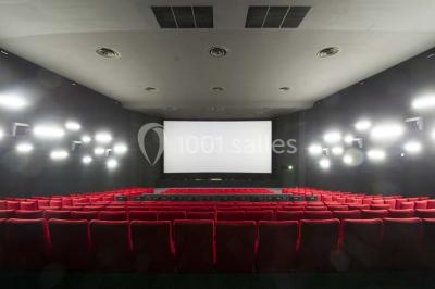 Salle vide avec moquette sombre, grande baie vitrée et structures métalliques visibles en arrière-plan.