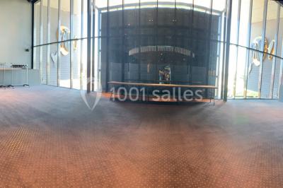 Salle vide avec moquette sombre, grande baie vitrée et structures métalliques visibles en arrière-plan.