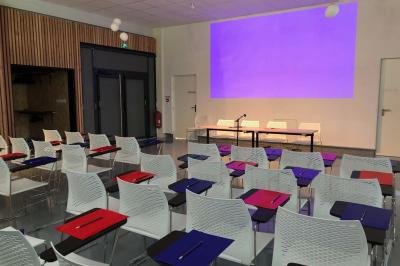 Salle de réception décorée avec des tables rondes, nappes blanches, serviettes orange et centres de table floraux.