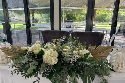 Salle de réception décorée avec des tables rondes, nappes blanches, serviettes orange et centres de table floraux.