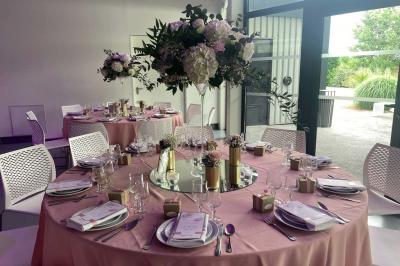 Salle de réception décorée avec des tables rondes, nappes blanches, serviettes orange et centres de table floraux.