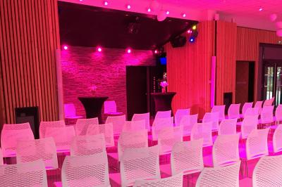 Salle de réception décorée avec des tables rondes, nappes blanches, serviettes orange et centres de table floraux.