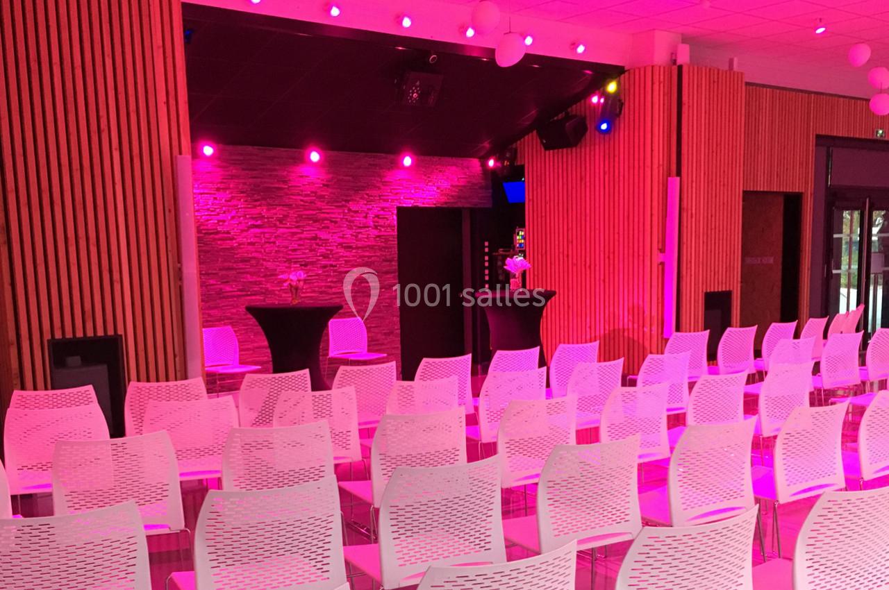 Salle de conférence avec des chaises blanches alignées, éclairage rose et un mur en pierre en arrière-plan.