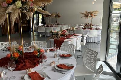 Salle de réception décorée avec des tables rondes, nappes blanches, serviettes orange et centres de table floraux.