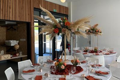 Salle de réception décorée avec des tables rondes, nappes blanches, serviettes orange et centres de table floraux.