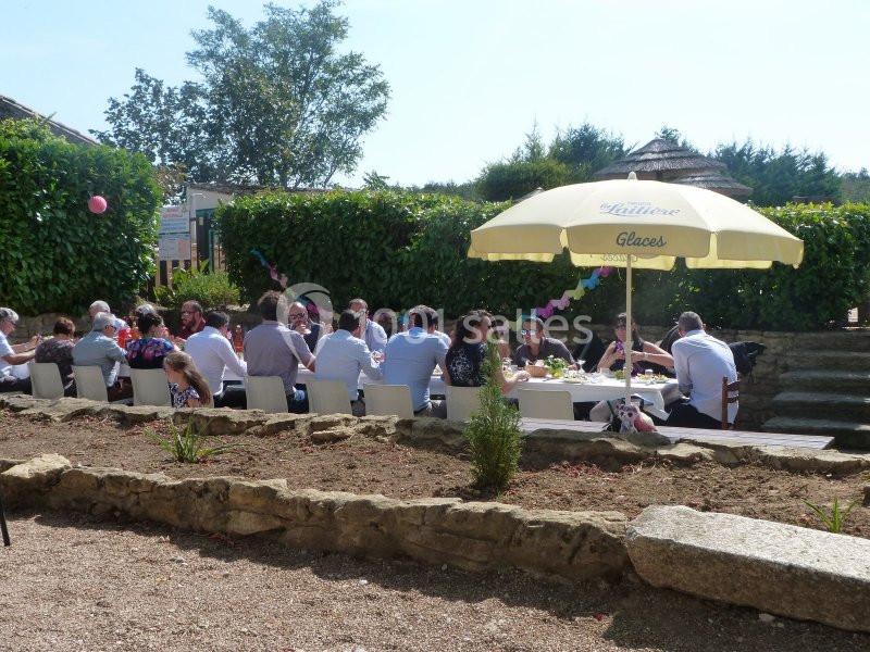 Groupe de personnes assises à une table en extérieur, sous un parasol, entourées de verdure et de décorations festives.