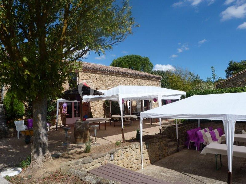 Tentes blanches installées dans une cour en pierre entourée d'arbres, avec des tables et chaises disposées pour un événement.
