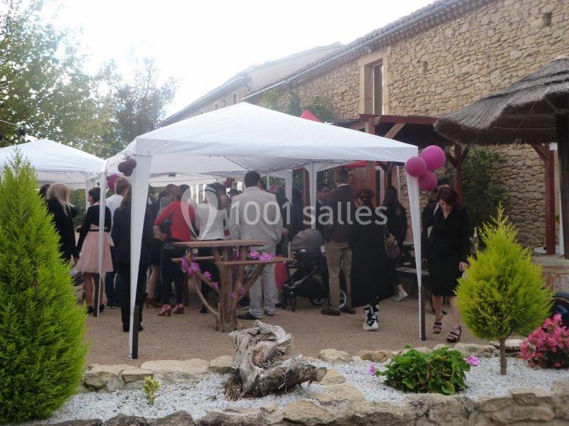 Groupe de personnes rassemblées sous des tonnelles blanches dans une cour extérieure près de bâtiments en pierre.