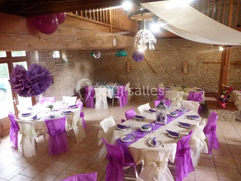 Salle de réception décorée avec des nappes blanches et des nœuds violets sur les chaises, prête pour un événement.