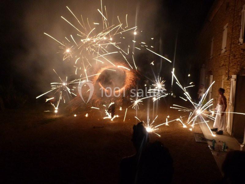 Des personnes observent un spectacle de feux d'artifice devant une maison en pierre, de nuit.