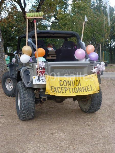 Un 4x4 décoré de ballons et d'une pancarte ’Convoi exceptionnel’ garé sur un terrain en plein air.