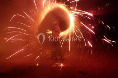 Personne manipulant un objet enflammé, créant des étincelles circulaires dans un environnement sombre.
