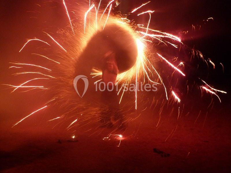 Personne manipulant un objet enflammé, créant des étincelles circulaires dans un environnement sombre.