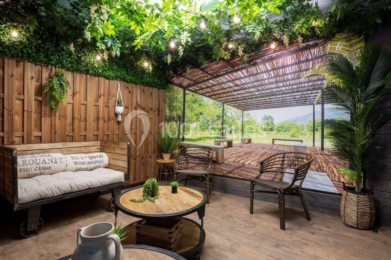 Espace intérieur décoré avec des plantes, des meubles en bois et un mur simulant une terrasse ouverte sur la nature.